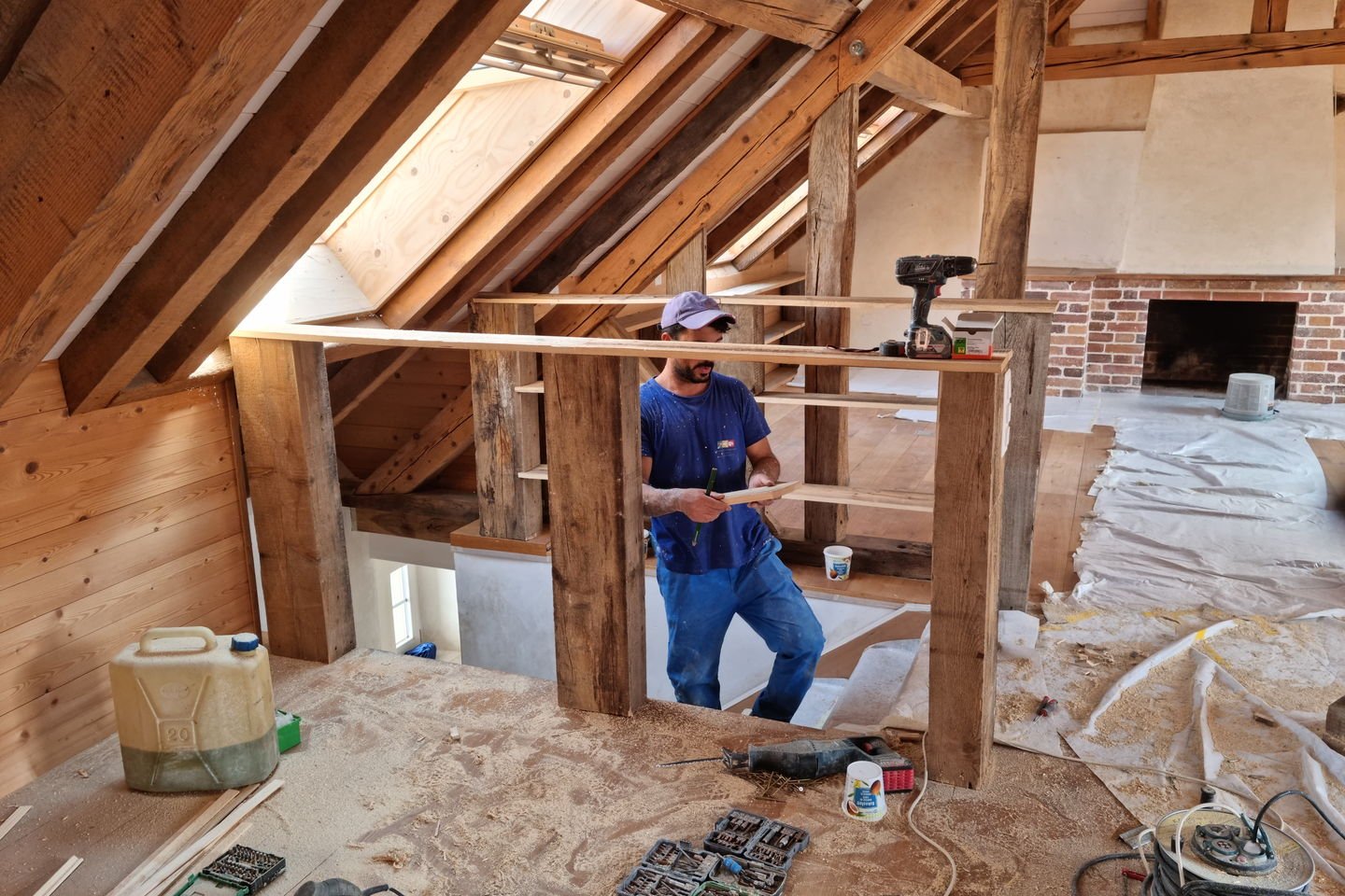 Menuisier en bleu de travail réglant une traverse du garde-corps dans les combles