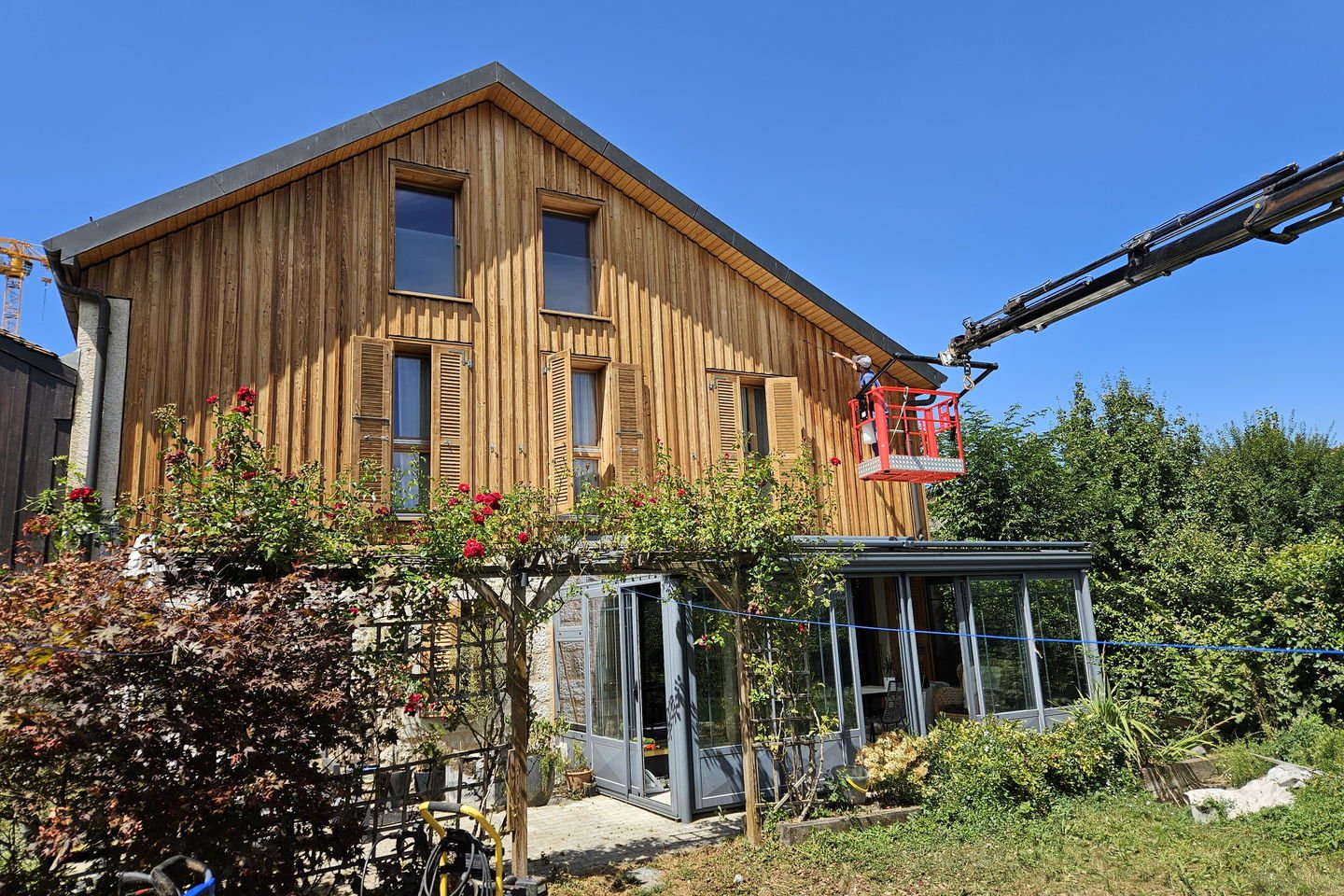 Maison au bardage bois avec un pignon en cours de traitement, une nacelle rouge à droite