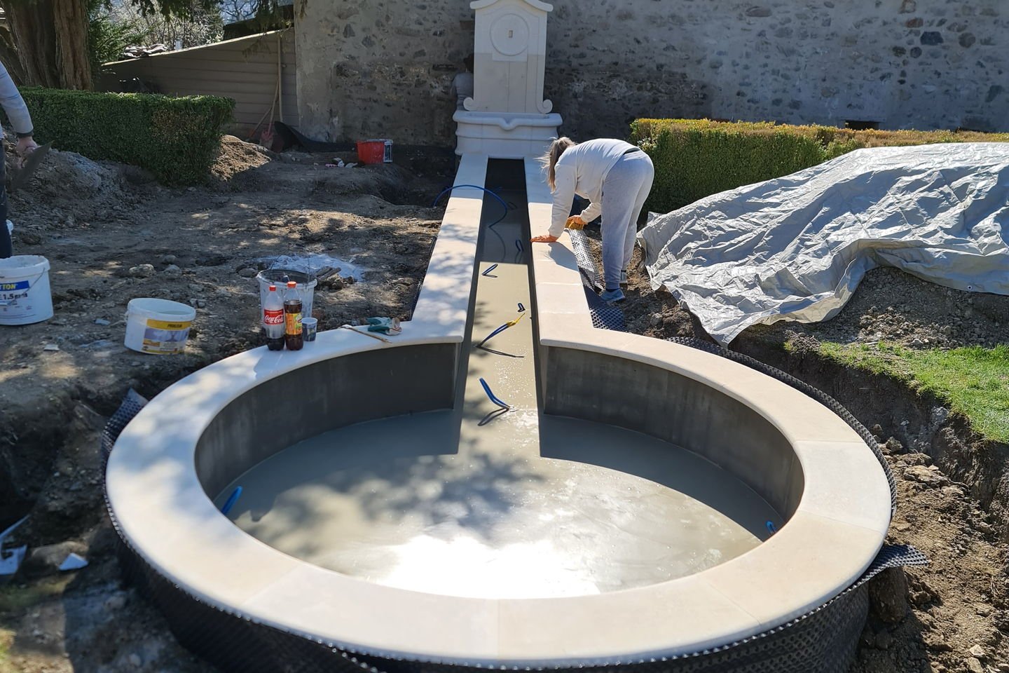 Vasque ronde en béton brut avec un pilier central, décoffrée, entourée de terre