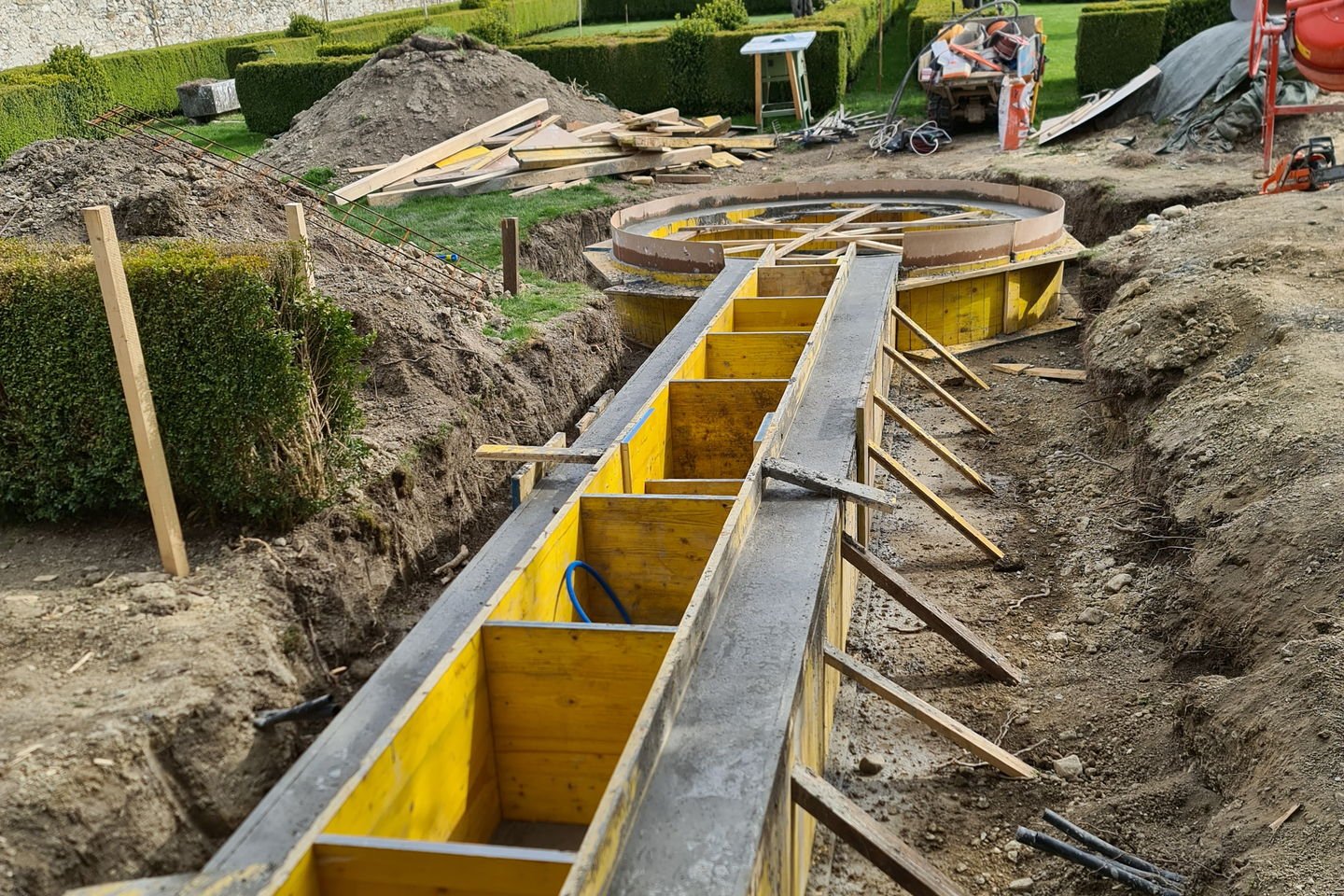 Longue banche droite en panneaux jaunes étayés, dans une tranchée le long d’un jardin