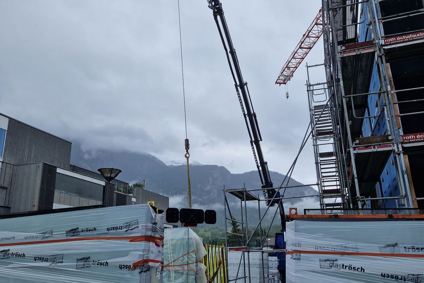 Camion-grue déchargeant des panneaux préfabriqués sur un chantier avec grue à tour