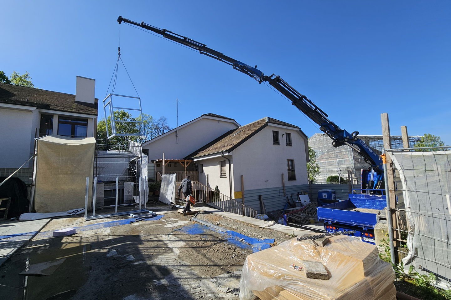 Camion-grue bleu, flèche déployée au-dessus des toits, sur un chantier bordé de maisons