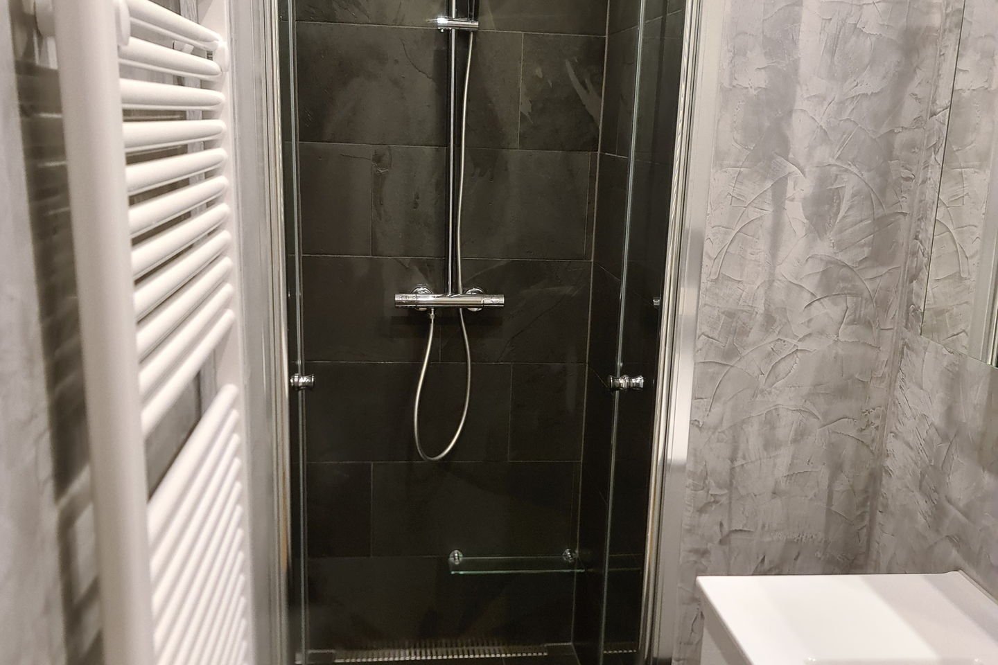 Douche à l’italienne de plain-pied avec paroi vitrée et sèche-serviettes blanc à côté