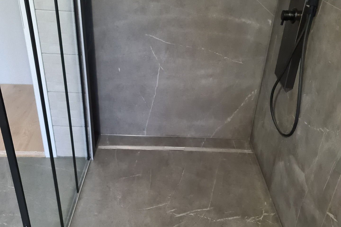 Mur de la douche en carrelage grand format effet marbre, avec colonne de douche encastrée
