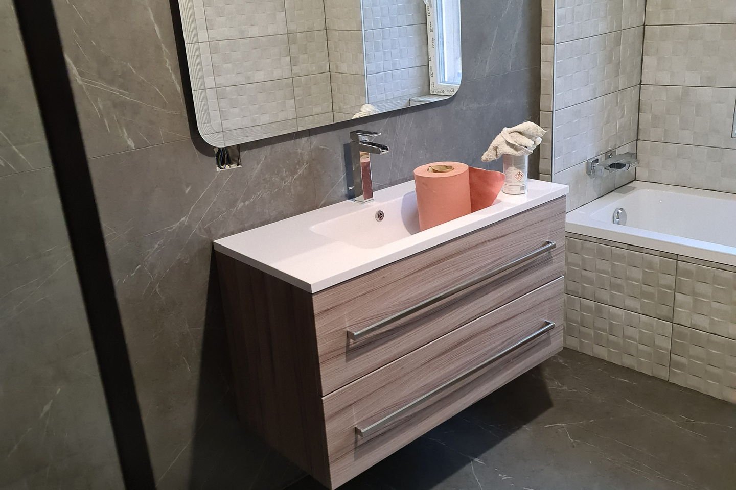 Salle de bains terminée : meuble vasque en bois suspendu, baignoire et murs en carrelage effet marbre gris