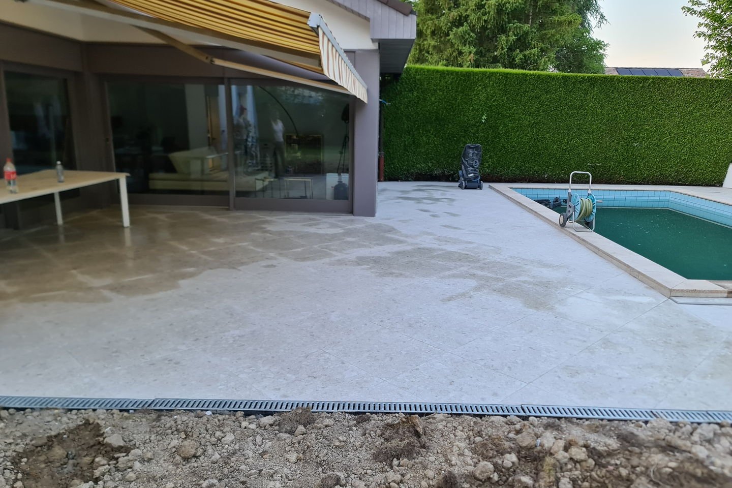 Angle de la plage carrelée avec le caniveau à grille en bordure et la terre encore ouverte