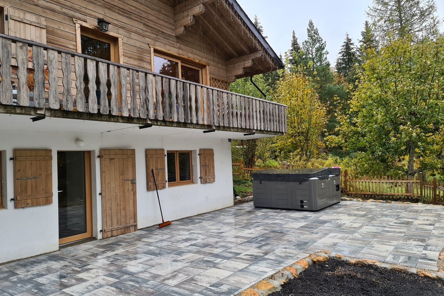 Terrasse en dalles grises devant un chalet en bois, avec un spa à droite et une bande de terre à planter
